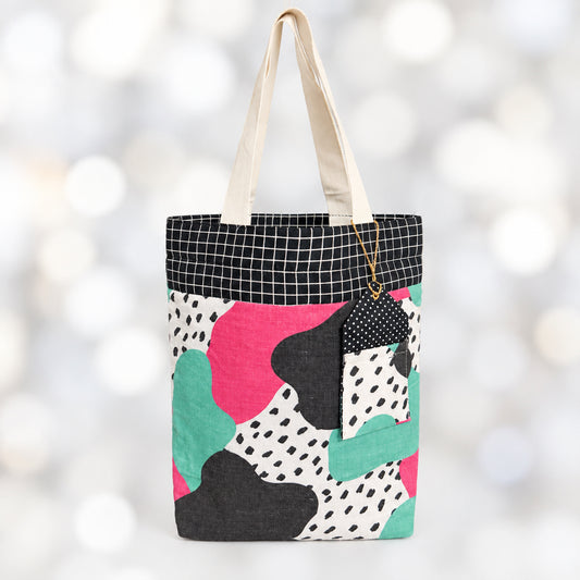 Reusable Fabric Gift Bag with matching gift tag holder in a abstract print and a blue checkered top border with white handles.
