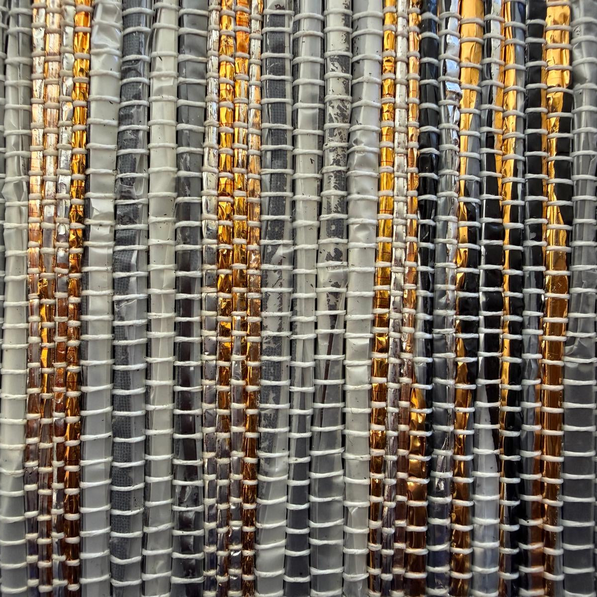 Close-up of a upcycled handwoven collapsible storage box small in gray, black, and gold weave.