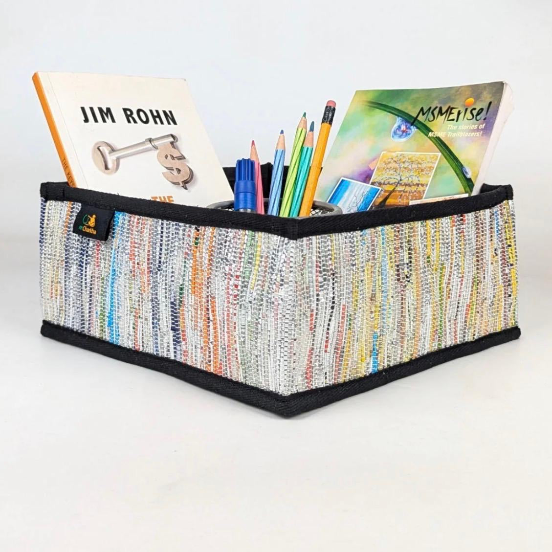 Upcycled handwoven multicolored collapsible storage basket with office supplies.