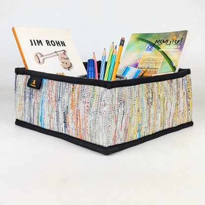 Upcycled handwoven multicolored collapsible storage basket with office supplies.
