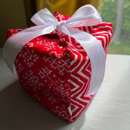 Reusable holiday gift box in a red & white snowflake & chevron print satin fabric, with a ribbon closure.