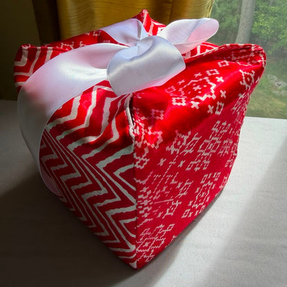 Reusable holiday gift box in a red & white snowflake & chevron print satin fabric, with a ribbon closure.