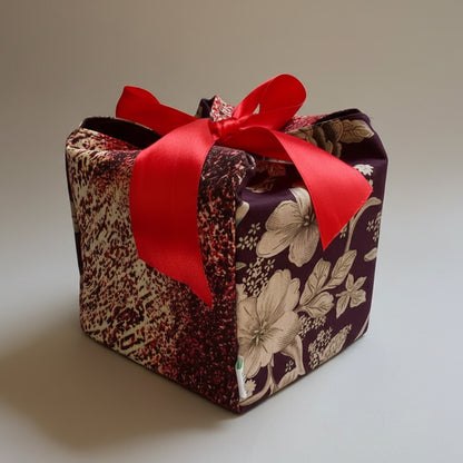 Wine colored floral & speckled fabric gift box with a rede ribbon closure in 7X7X7 square size.