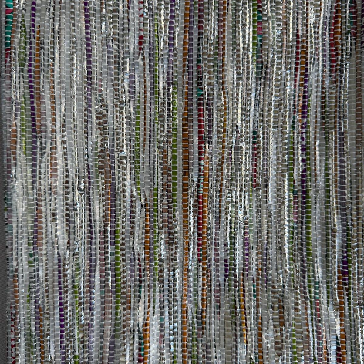 Close-up of upcycled handwoven Sling-It Bag in multicolored silver weave with a grey strap.